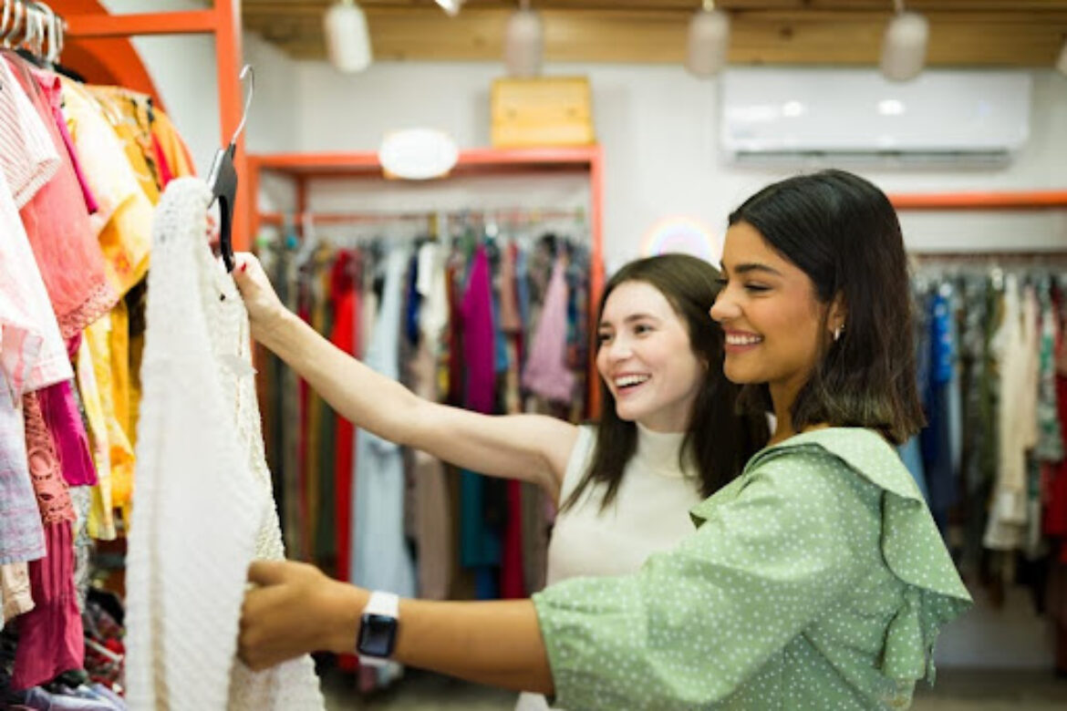 Young women holding up a piece of clothing to look at from a thrift store rack