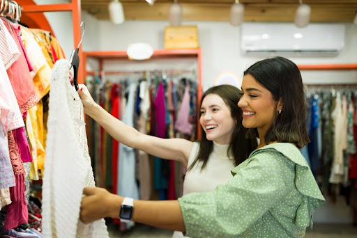 Young women holding up a piece of clothing to look at from a thrift store rack