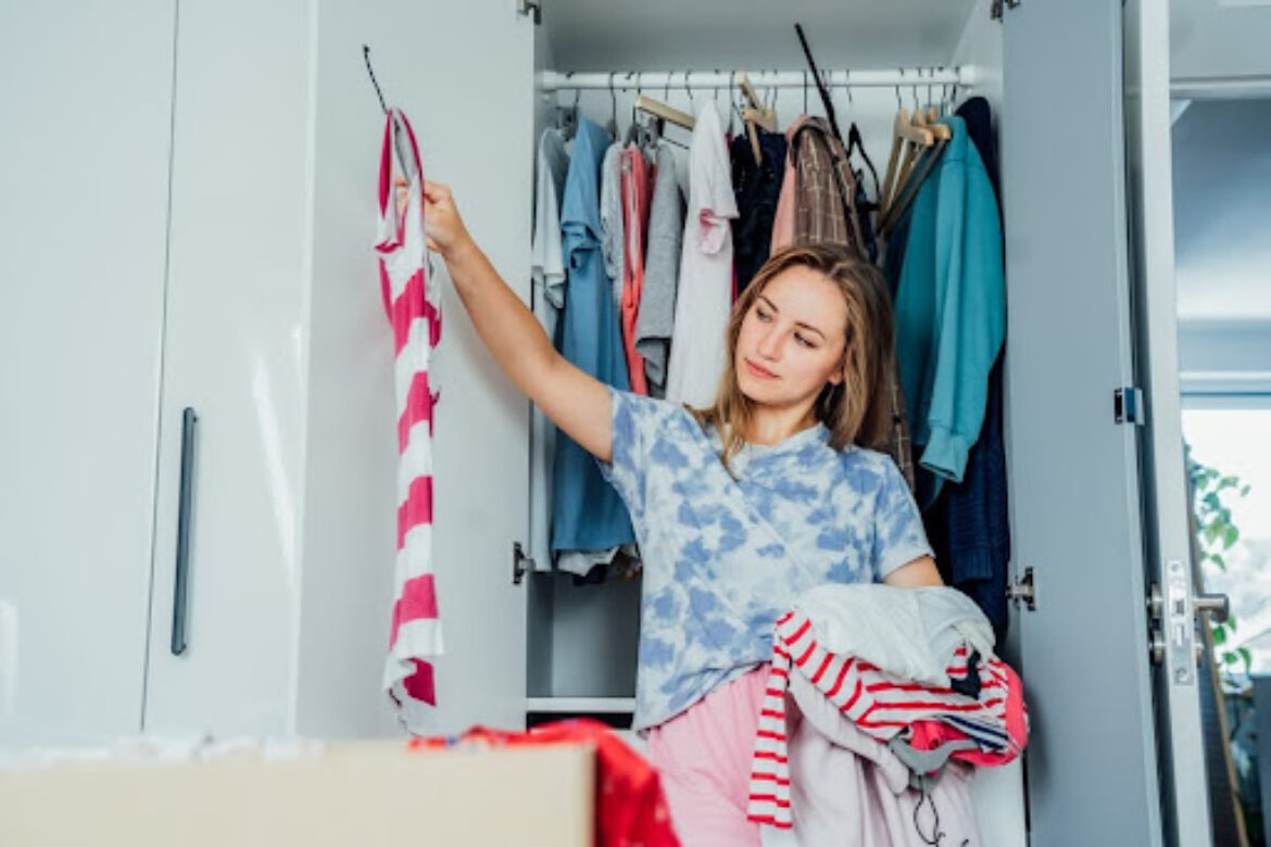 woman holding up a shirt from a few hangers of clothes