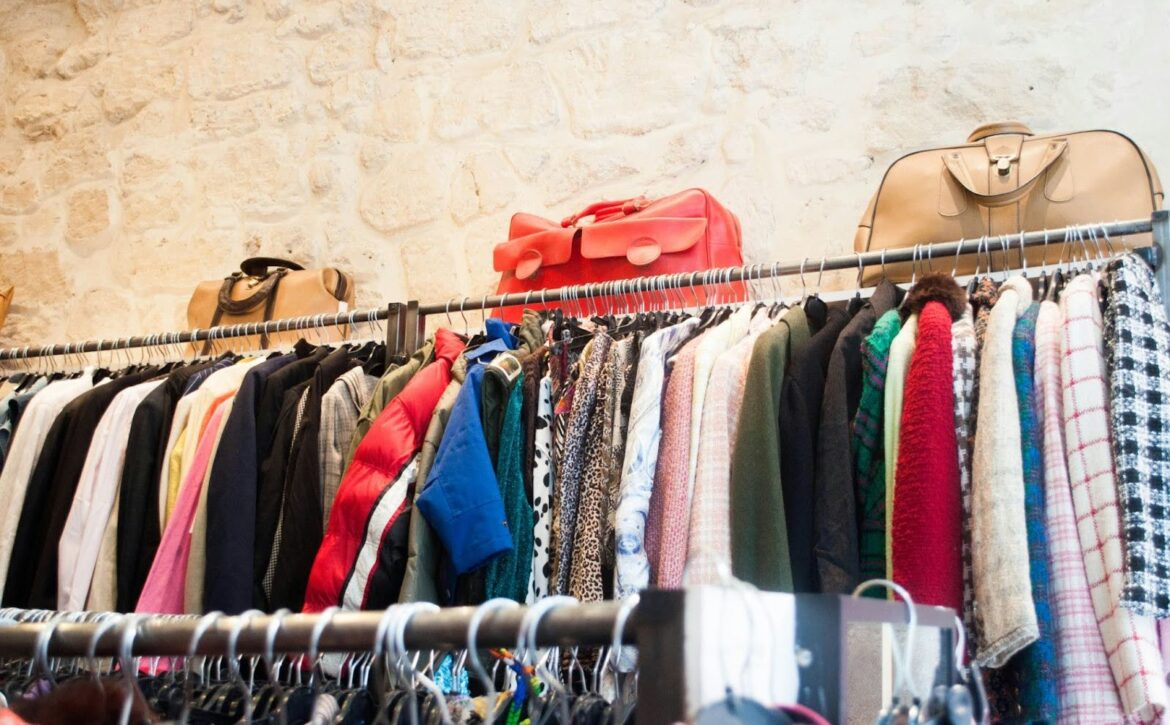 clothes racks along a brick textured wall with the racks topped with a selection of purses