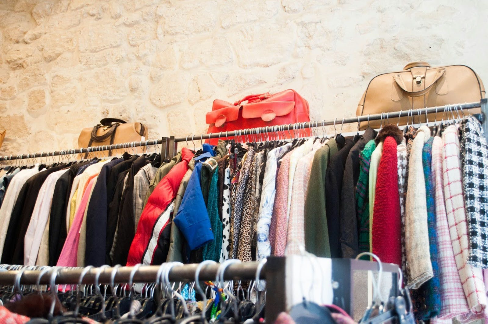 clothes racks along a brick textured wall with the racks topped with a selection of purses